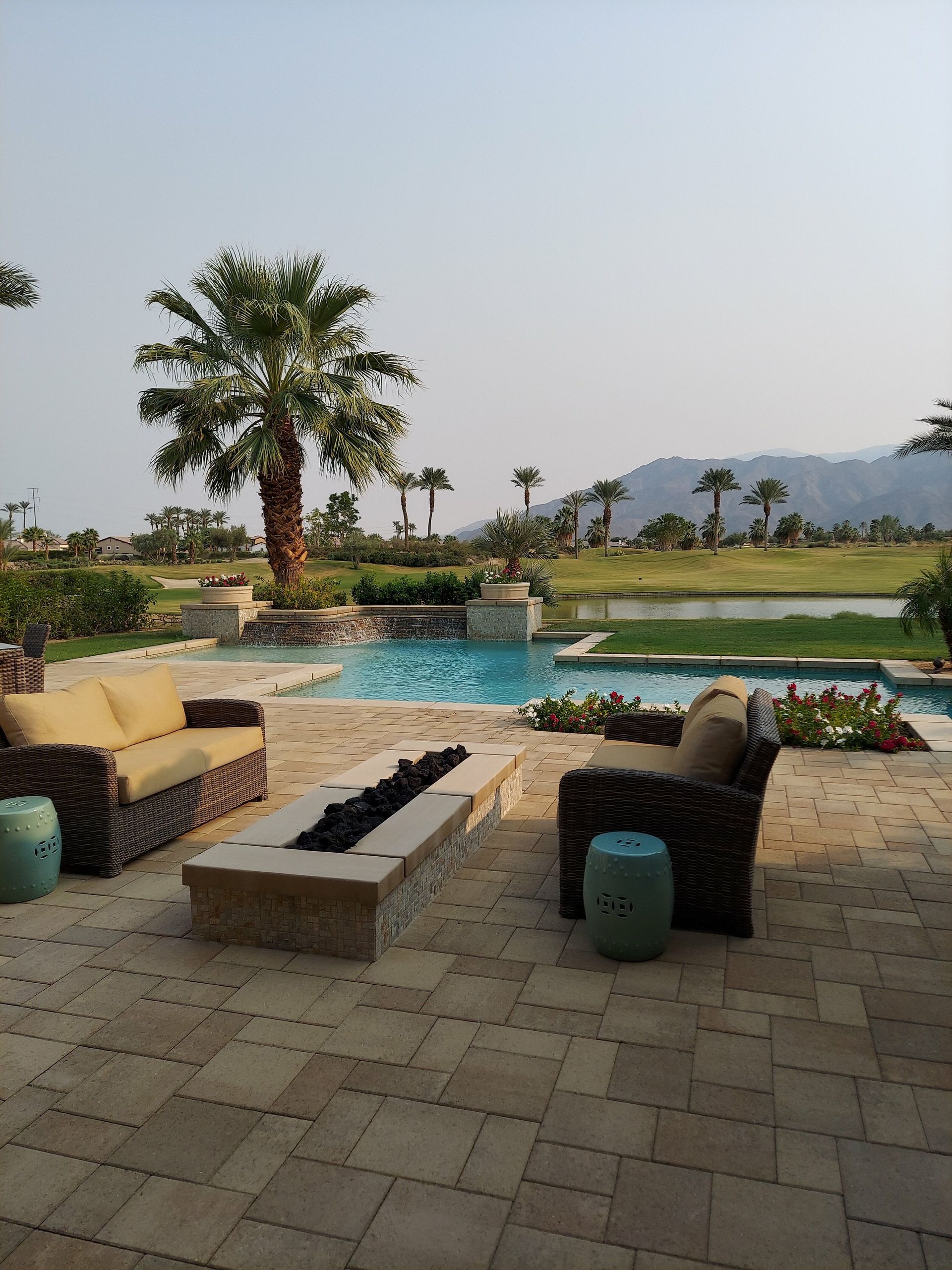 Sunny outdoor patio with poolside view, palm trees, and cozy seating at a tropical resort.